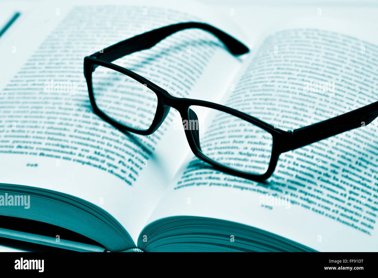 Libre d'une paire de lunettes cerclées de noir en plastique sur un livre ouvert, en duotone Banque D'Images