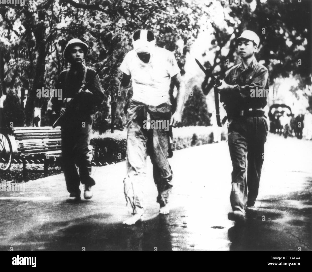 Guerre du Vietnam. NParading /de prisonnier, avec visage bandé, marche pieds nus entre deux gardes Vietcong. Banque D'Images