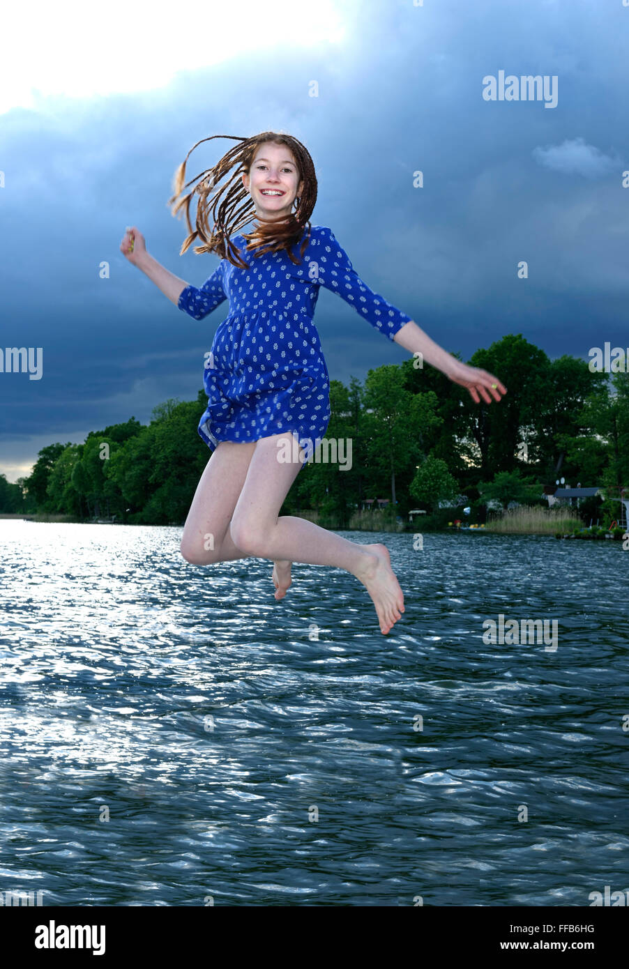 Fille de sauter dans l'eau avec dress on, des nuages sombres, Ellbogensee supérieure, Havel, Priepert, Mecklenburg Lake District Banque D'Images