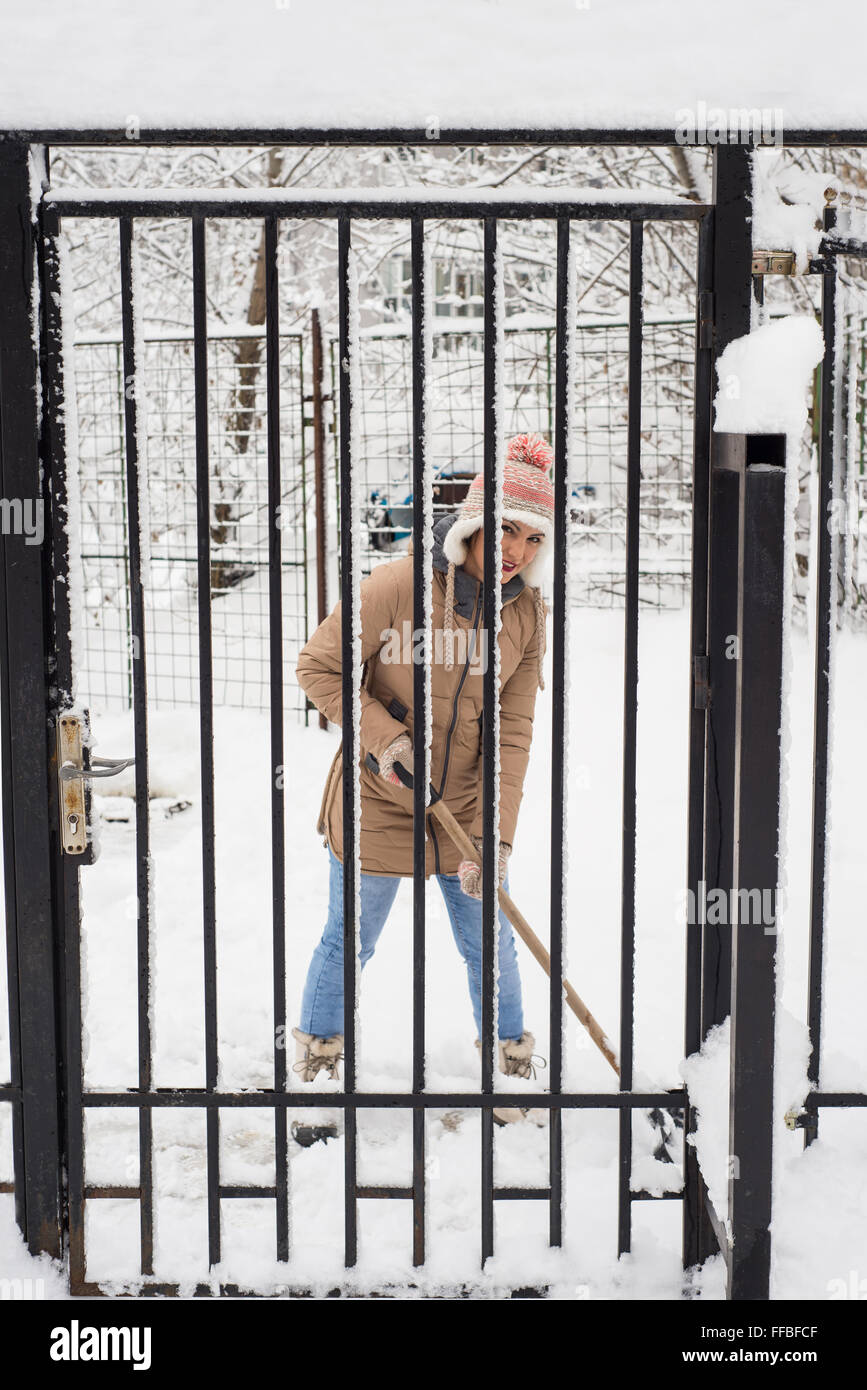 Femme de pelleter de la neige par une clôture et souriant Banque D'Images