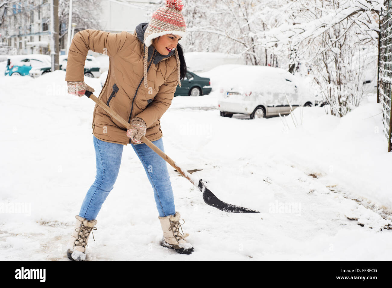 Happy woman pelleter la neige dans parking autour de house Banque D'Images