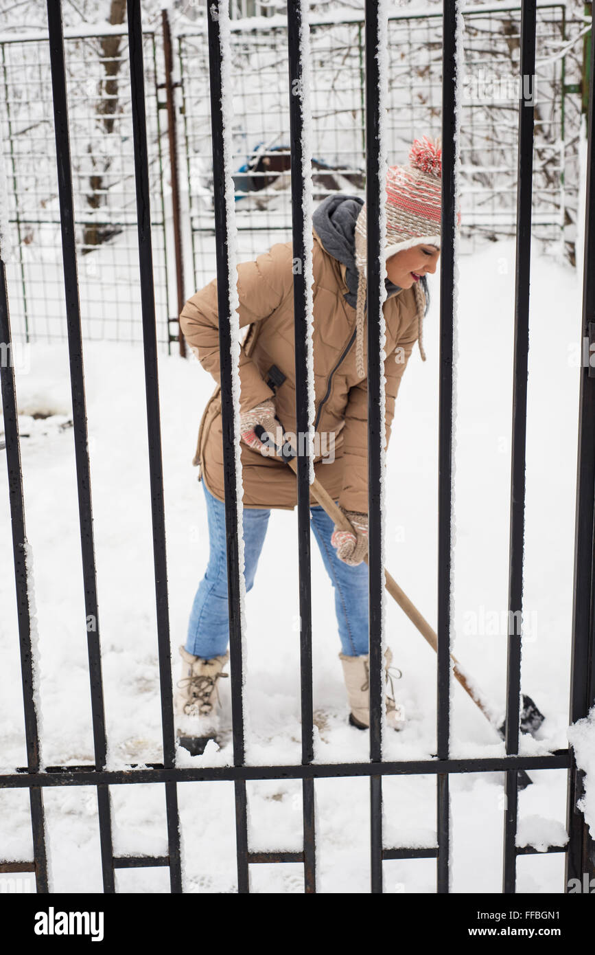 Femme qui travaille avec pelle à neige by fence Banque D'Images