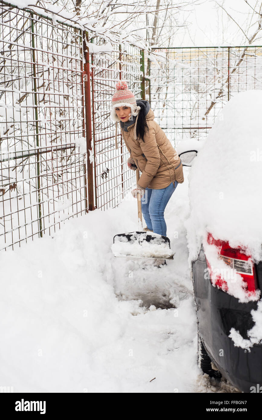 Femme de pelleter de la neige autour de voiture dans une journée froide Banque D'Images