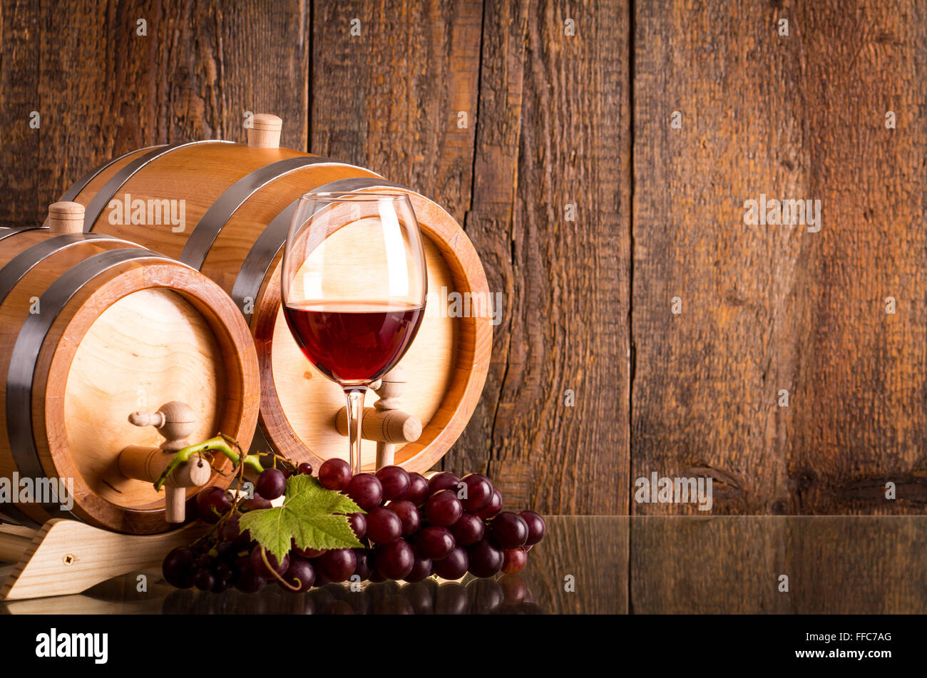 Verre de vin rouge avec deux barils en bois foncé et raisins background Banque D'Images