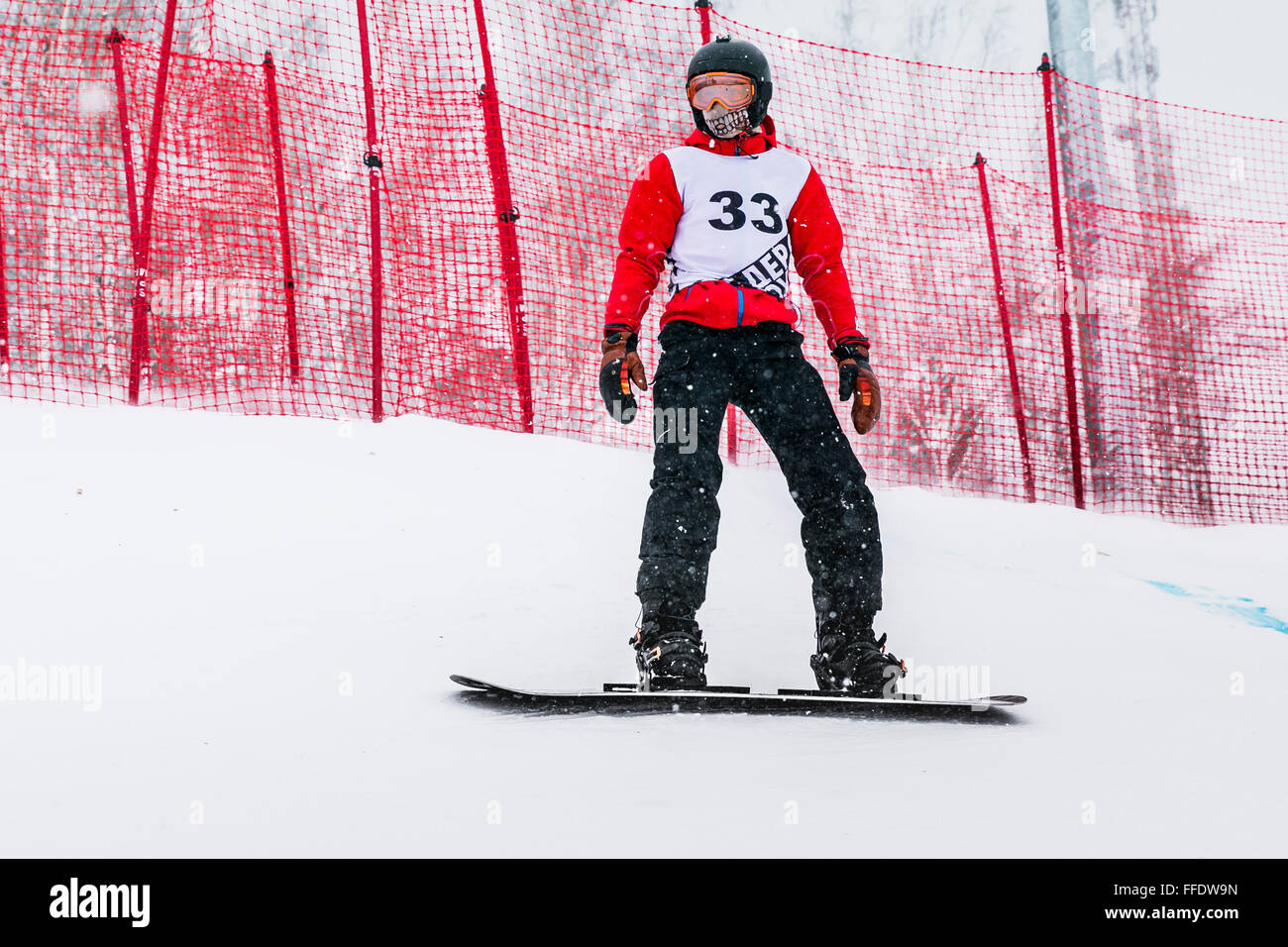 Jeune athlète homme snowboarder durant la compétition s'arrête sur la pente de montagne Banque D'Images