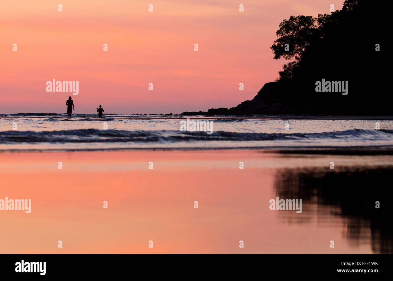 Deux personnes debout dans la mer au coucher du soleil sur une plage dans l'ouest de Sabah, Malaisie Banque D'Images