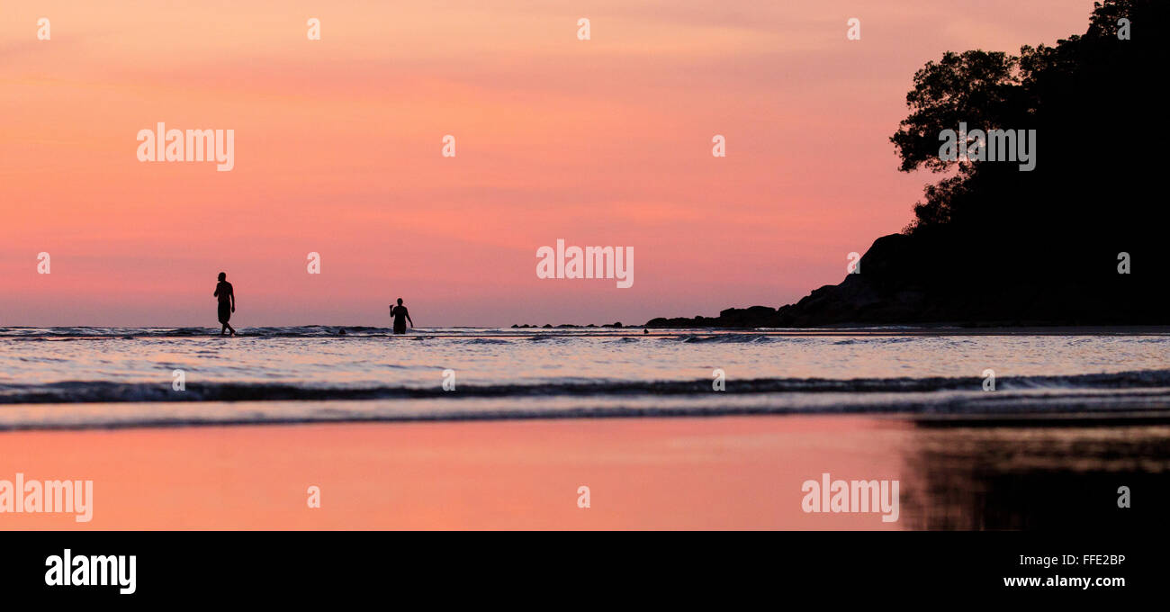 Deux personnes debout dans la mer au coucher du soleil sur une plage dans l'ouest de Sabah, Malaisie Banque D'Images