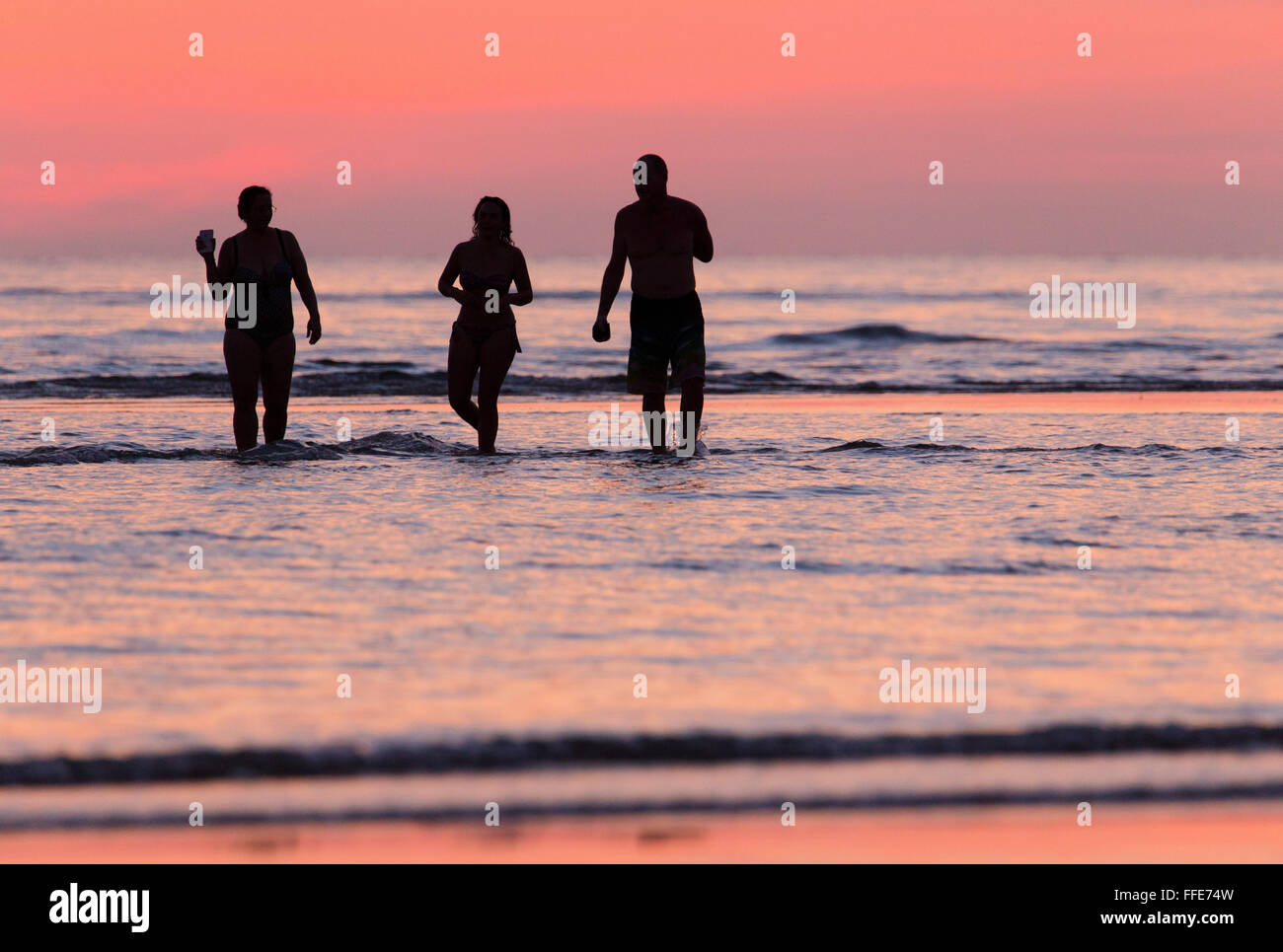 Trois personnes debout dans la mer au coucher du soleil sur une plage dans l'ouest de Sabah, Malaisie Banque D'Images