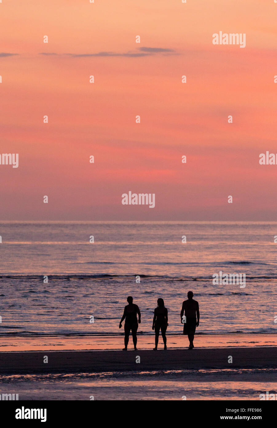 Silhouette de trois personnes debout par la mer au coucher du soleil sur une plage dans l'ouest de Sabah, Malaisie Banque D'Images