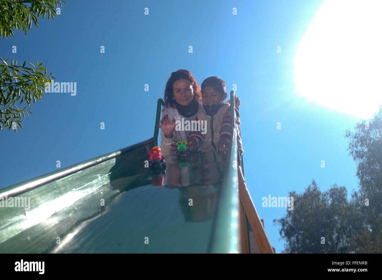 Cochabamba, Bolivie. Caucasian woman avec son garçon adopté d'Amérique latine s'amusant jeu de plein air à la diapositive de maternelle Banque D'Images