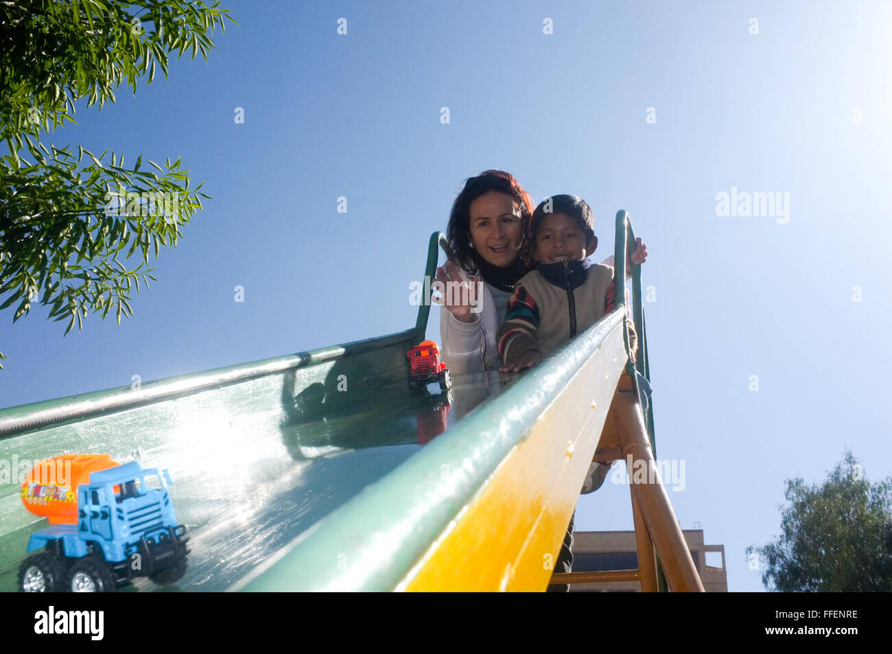 Cochabamba, Bolivie. Caucasian woman avec son garçon adopté d'Amérique latine s'amusant jeu de plein air à la diapositive de maternelle Banque D'Images