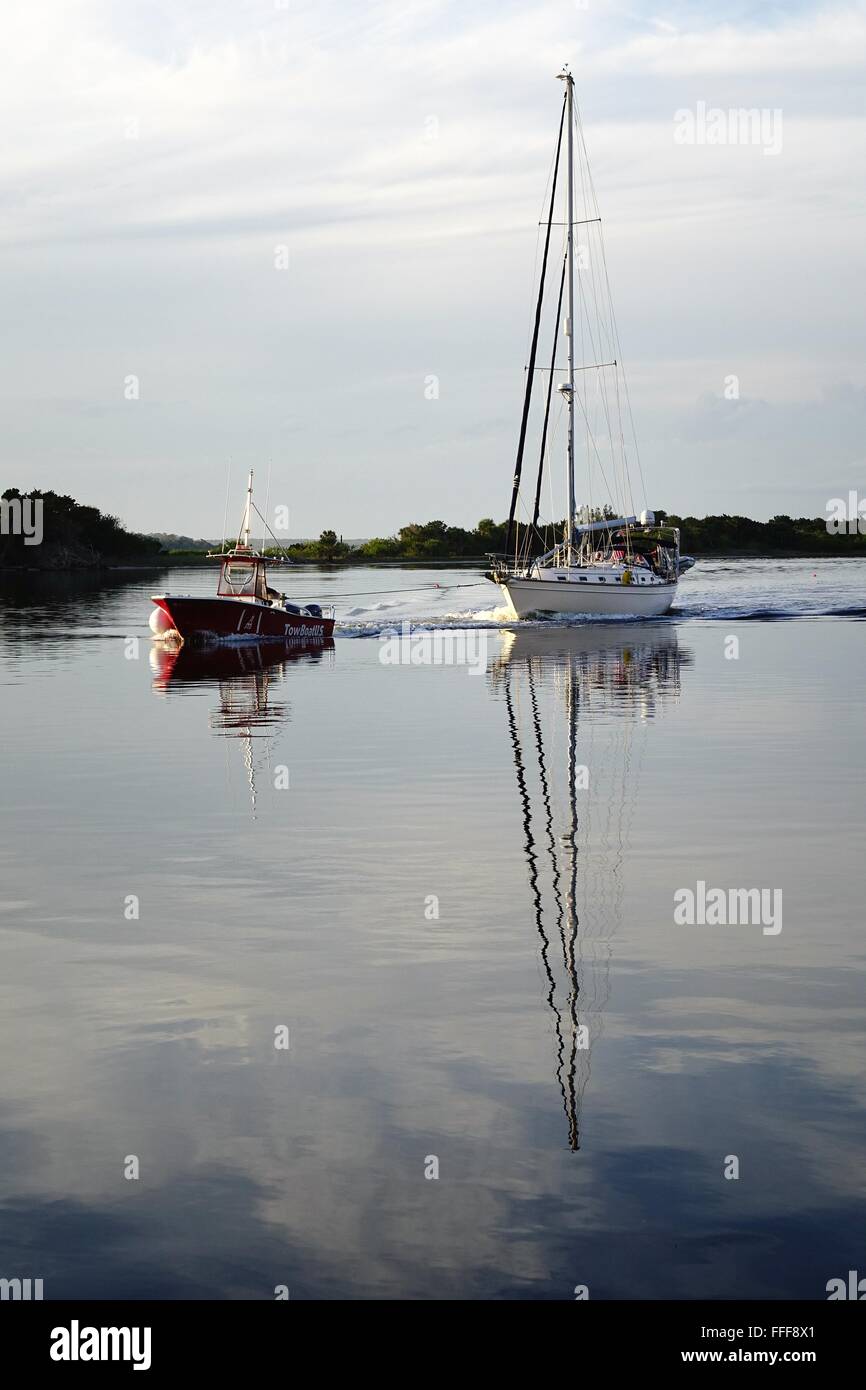 Bateau-remorqueur tirant une mobilité voilier sur la rivière d'Halifax, en Floride Banque D'Images