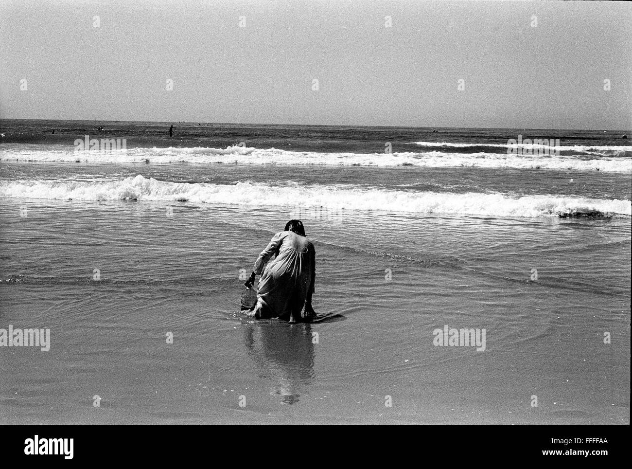 Jan 4, 2016 - South Beach, KwaZulu-Natal, Afrique du Sud - une femme s'agenouille sur le sable humide, la collecte de l'eau de mer pour l'auto-guérison. South Beach est une partie de la ville de Durban sans interruption la plus longue étendue de plage de sable. La ville de Durban est sur la côte est de l'Afrique du Sud et les gens ici sont lavés avec de l'eaux chaudes de l'Océan Indien. Au nord de cette étendue de sable sont des plages avec la société hang out cafe. Au sud il y a une jetée avec le quartier haut Moyo's Restaurant à elle est la fin et l'uShaka Marine World et le secteur complexe de la mer et surf clubs de la vesces Banque D'Images