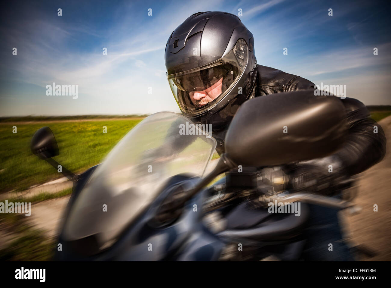 Biker dans casque et blouson de cuir racing sur la route Banque D'Images
