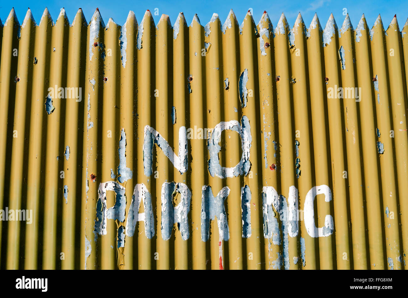 Un livre blanc 'No Parking sign' est peint sur une clôture de fer ondulé jaune. Banque D'Images