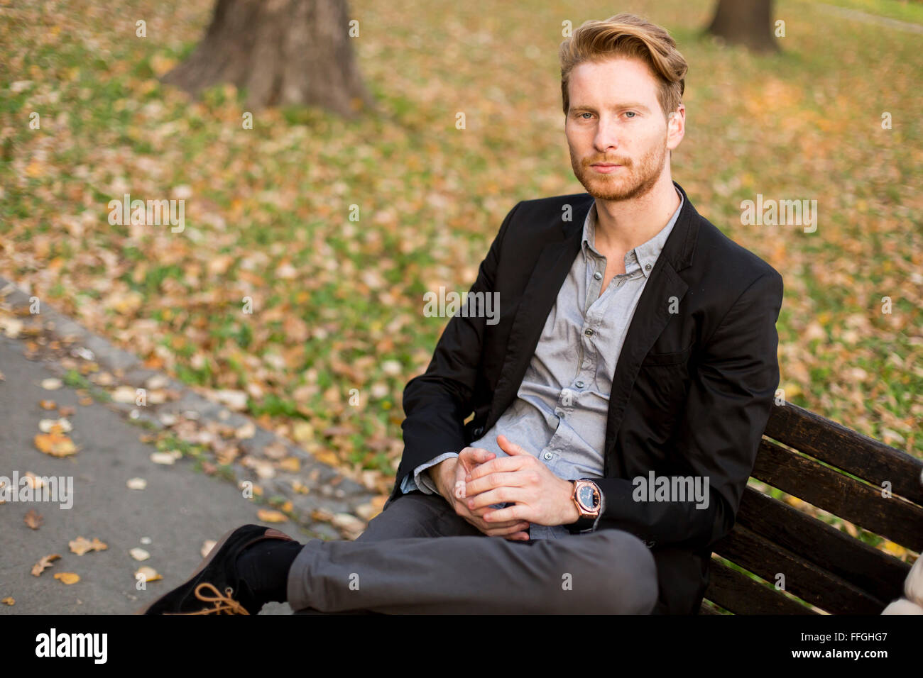Jeune homme sur un banc de parc à l'automne Banque D'Images