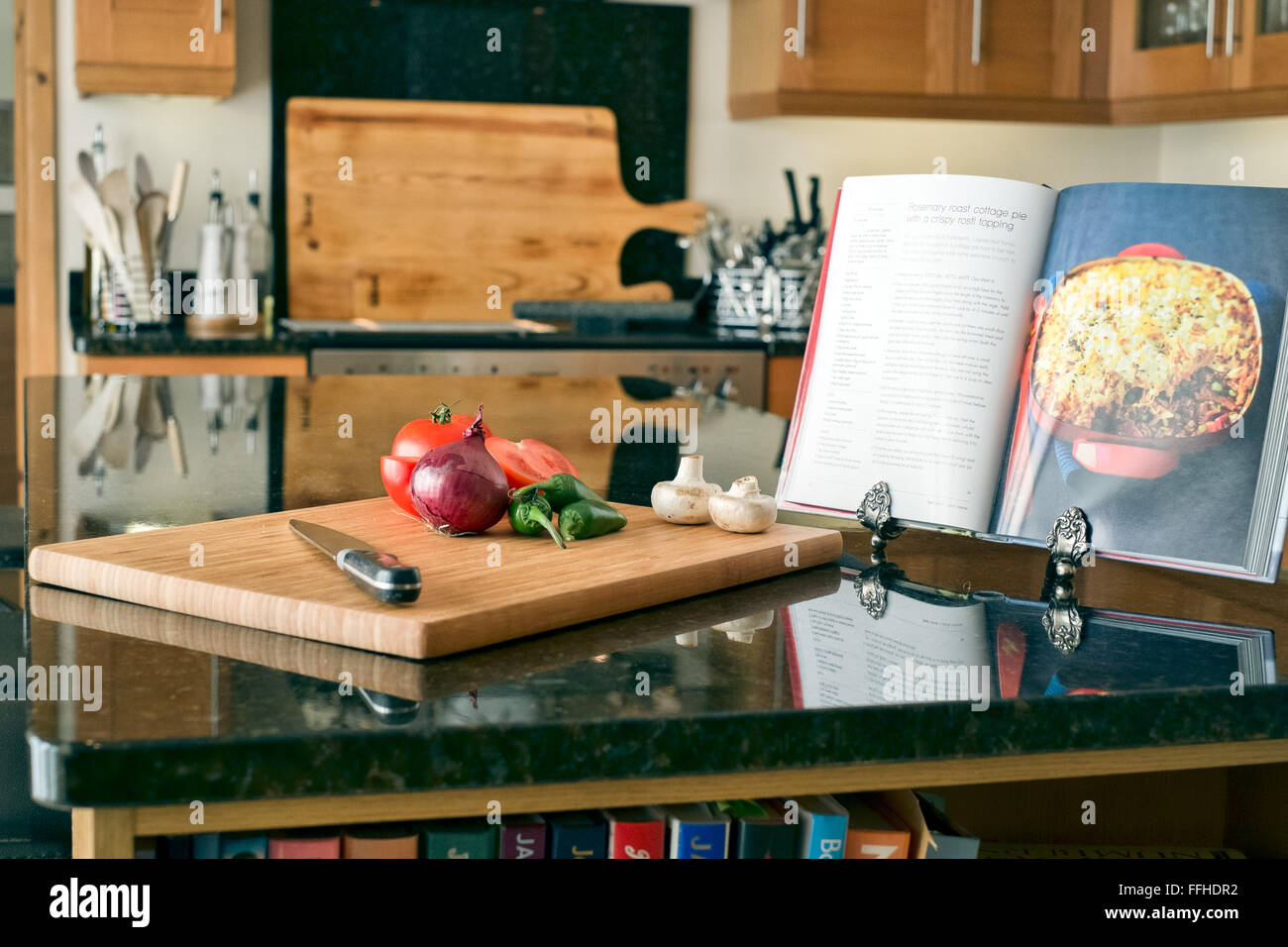 La préparation des aliments dans une cuisine domestique à l'aide d'une planche à découper, couteau et livre de recettes Banque D'Images