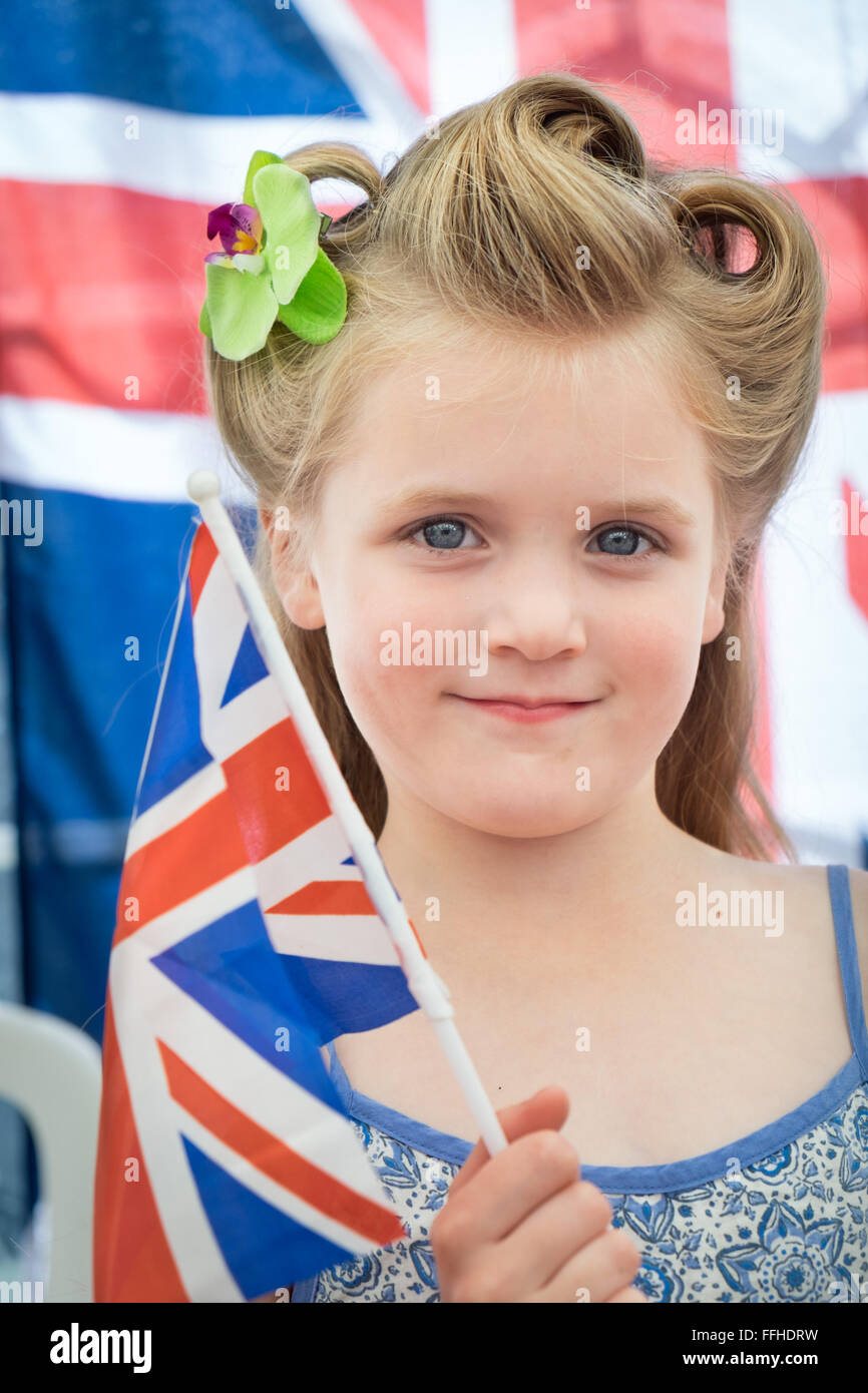 Une jeune fille blonde avec ses cheveux dans un style des années 1940 montrant le patriotisme, tenant un drapeau de l'union à un événement vintage Banque D'Images