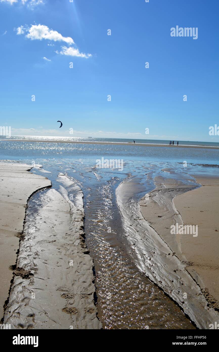 Flux d'eau douce dans une mer à marée basse à Camber Sands dans le Sussex, Angleterre, avec kite surfeurs en mer Banque D'Images