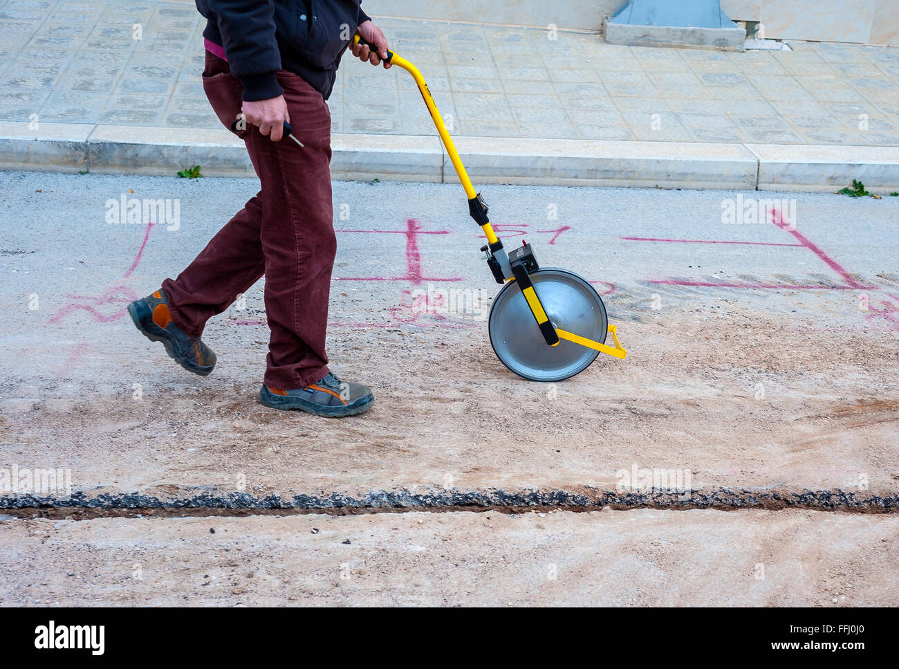 Surveyor avec roue à mesurer (odomètre) détecte la longueur d'une excavation de minitrench Banque D'Images