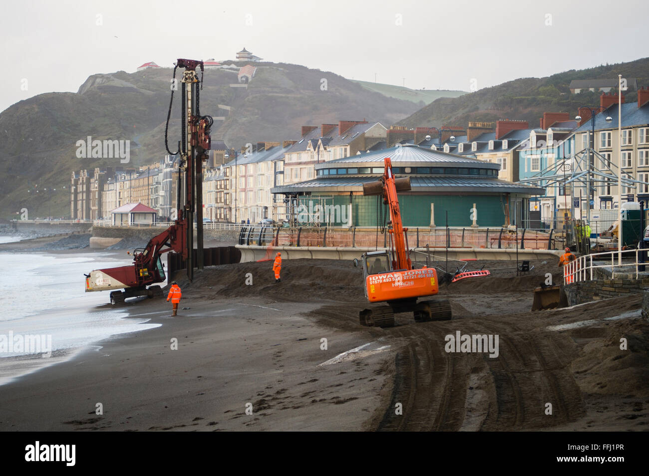 Les travailleurs de la construction de retirer la barrière de protection en acier du nouveau kiosque sur la promenade d'Aberystwyth, à l'aide de chenilles Caterpillar des machines des lourds, le Pays de Galles UK Banque D'Images