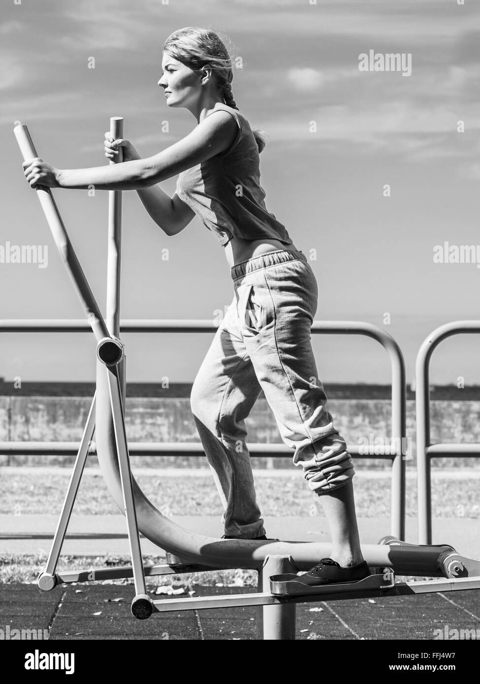 Jeune femme active exerçant sur la machine elliptique. Monter fille sportive dans la formation suit l'élaboration à la salle de sport en plein air. Sport Banque D'Images