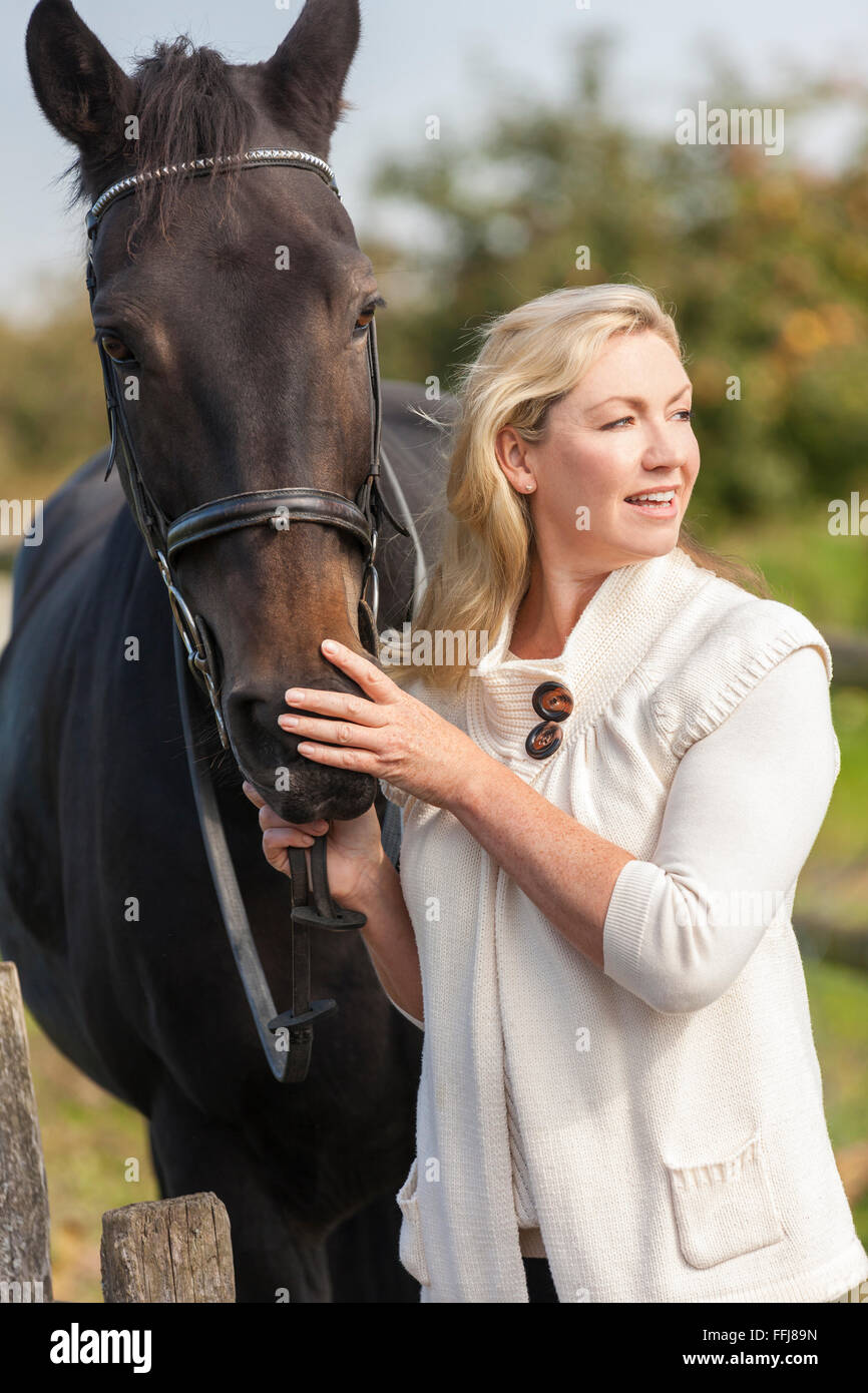 Beautiful happy young woman smiling et caresser son cheval à l'extérieur dans le champ ensoleillé Banque D'Images