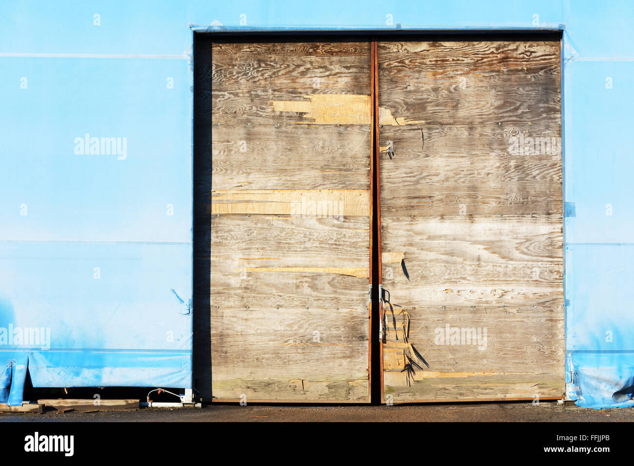 Une porte en bois patiné et cassée sur un entrepôt en plastique temporaire. Banque D'Images