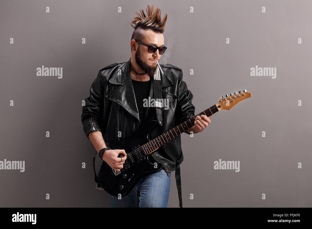 Jeune punk rocker fumer une cigarette et de jouer la guitare électrique contre un mur gris Banque D'Images