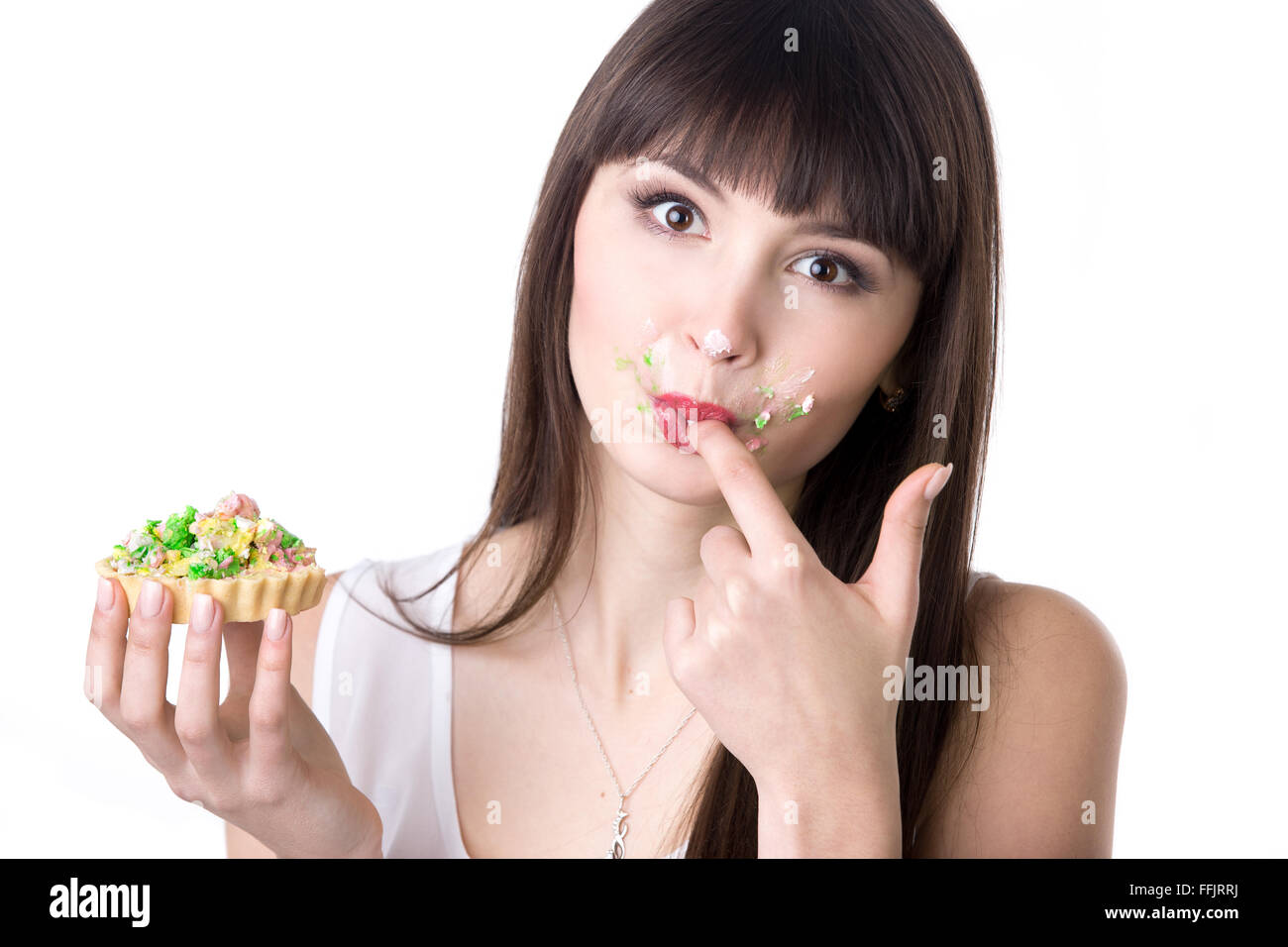 Young attractive woman faim ludique lécher ses doigts couverts de crème tout en mangeant très savoureux gâteau tarte. Studio Banque D'Images