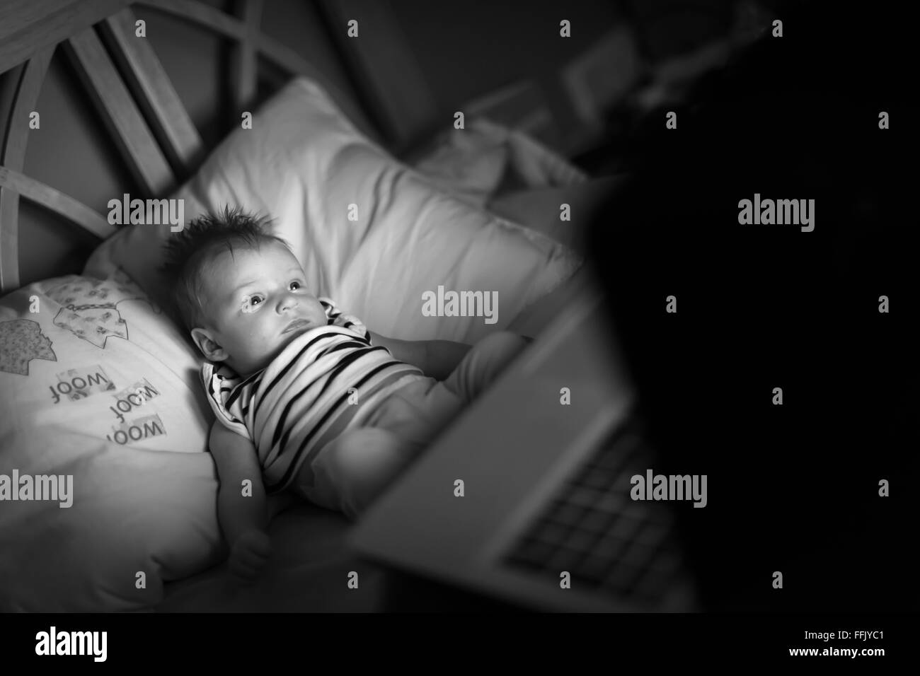Photographie en noir et blanc d'un bébé couché sur un oreiller à la recherche à un ordinateur portable Banque D'Images