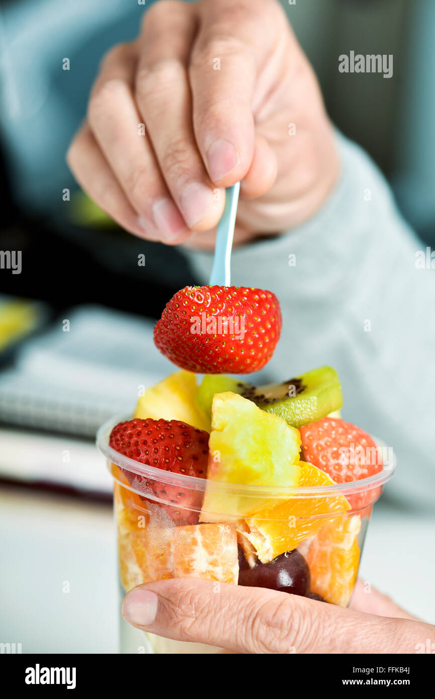 Libre d'un jeune homme de race blanche de manger une salade de fruits à partir d'une tasse en plastique transparent à l'office Banque D'Images