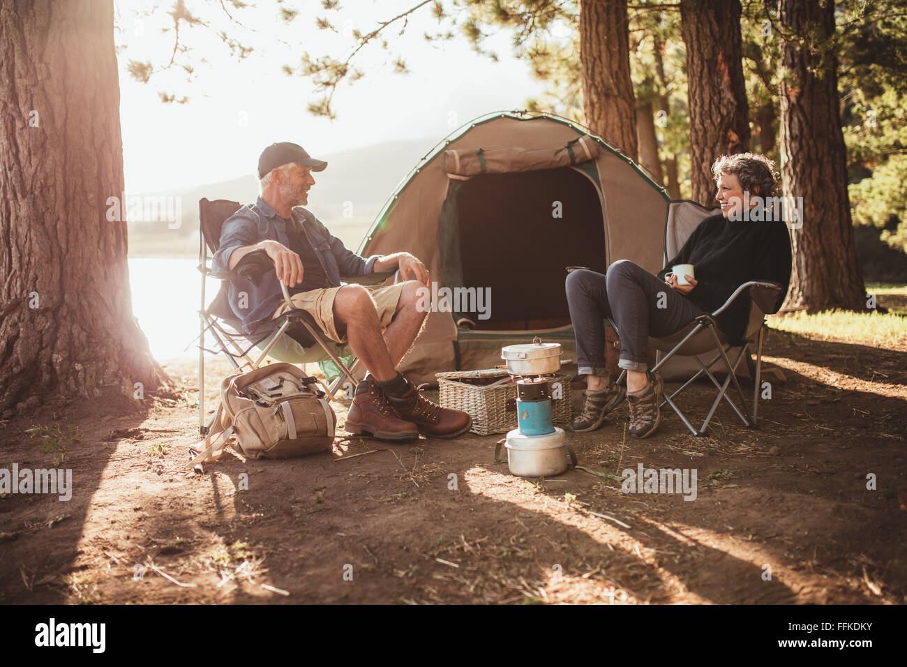 Portrait of happy senior couple sitting in chaises par tente au camping. Man and Woman relaxing et parler près d'un lac sur Banque D'Images