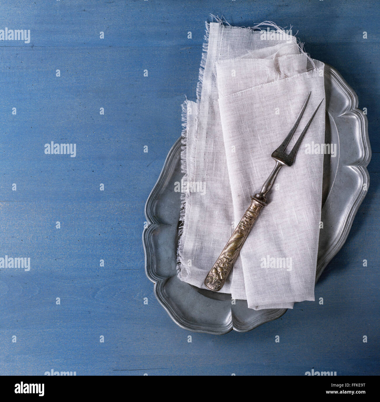Plaque métal vintage vide avec blanc textil serviette et fourchette à viande plus grande surface en bois bleu. Vue d'en haut. Image carré Banque D'Images