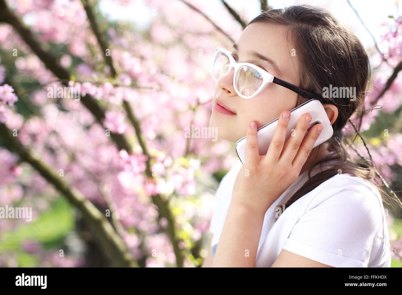 A girl talking on a cell phone alors qu'il se tenait sous un arbre fleuri. Appel téléphonique. Girl with mobile phone Banque D'Images