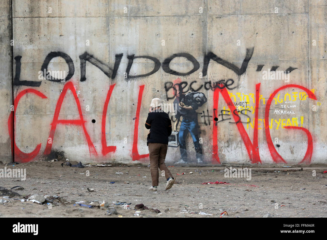 Calais, France. 10 fév, 2016. Un homme passe par les graffiti 'LONDON CALLING' phoning sur son smartphone. L'emblématique graffiti Banksy, près du camp de migrants de Calais connu comme 'La Jungle' a été vandalisé par les mots 'London Calling'. Les mots "London Calling" en lettrage géant sur le haut de l'image - à l'aide de la figure de Steve Jobs comme le 'je'. Banque D'Images