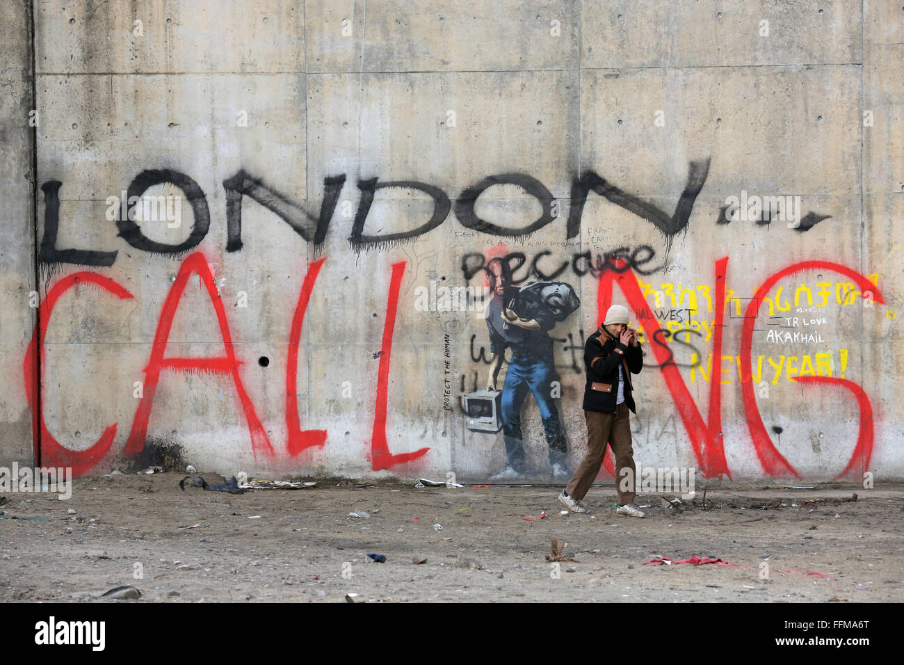 Calais, France. 10 fév, 2016. Un homme passe par les graffiti 'LONDON CALLING' phoning sur son smartphone. L'emblématique graffiti Banksy, près du camp de migrants de Calais connu comme 'La Jungle' a été vandalisé par les mots 'London Calling'. Les mots "London Calling" en lettrage géant sur le haut de l'image - à l'aide de la figure de Steve Jobs comme le 'je'. Banque D'Images