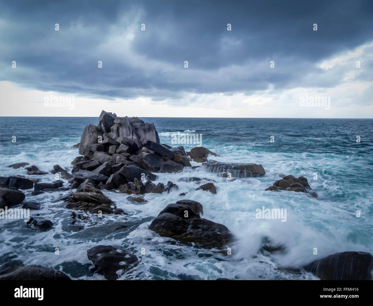 Les vagues déferlent sur les rochers, avec de sombres nuages frais généraux qui se profile Banque D'Images