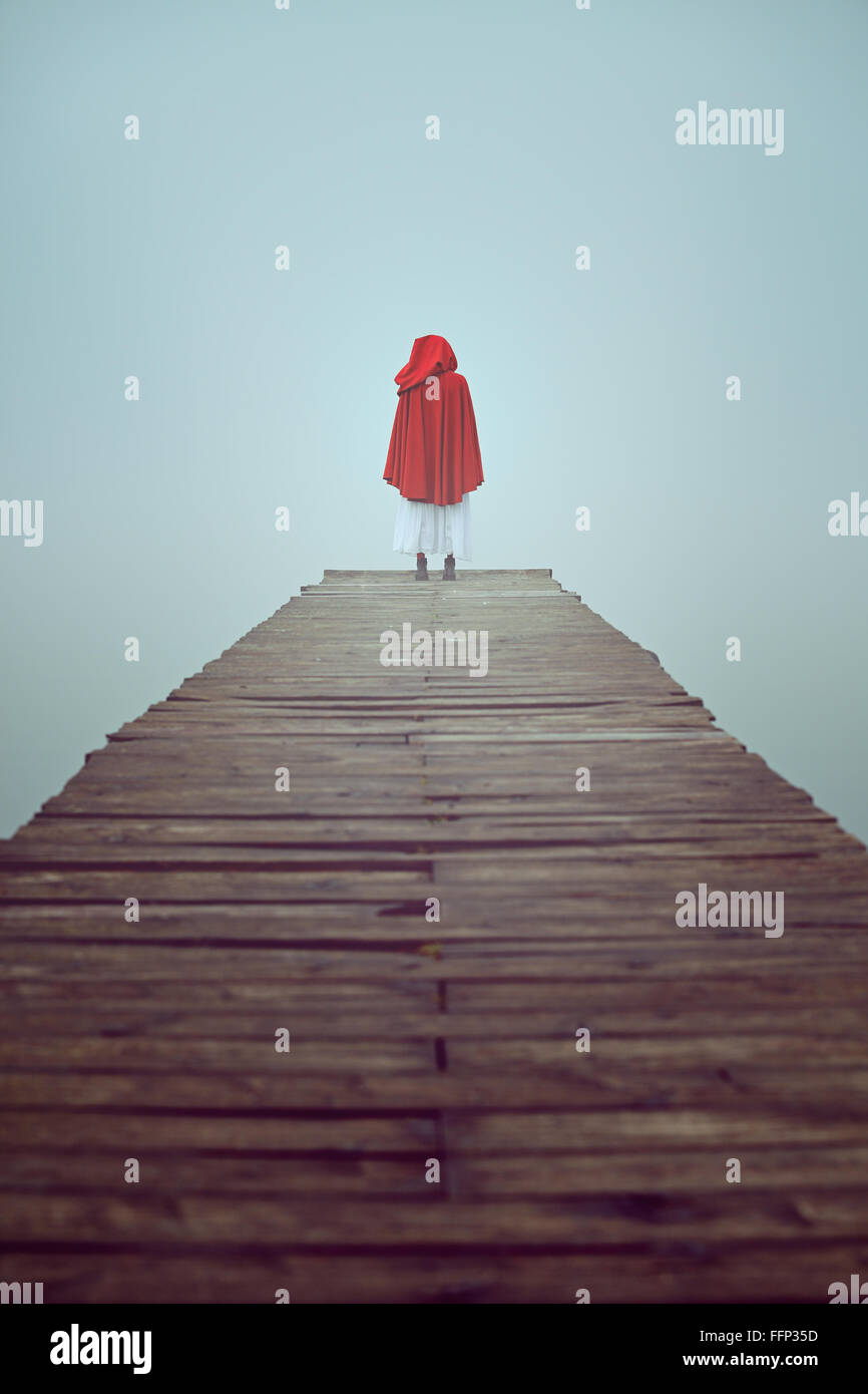 Femme seule habillée d'une robe à capuchon rouge dans un misty pier Banque D'Images
