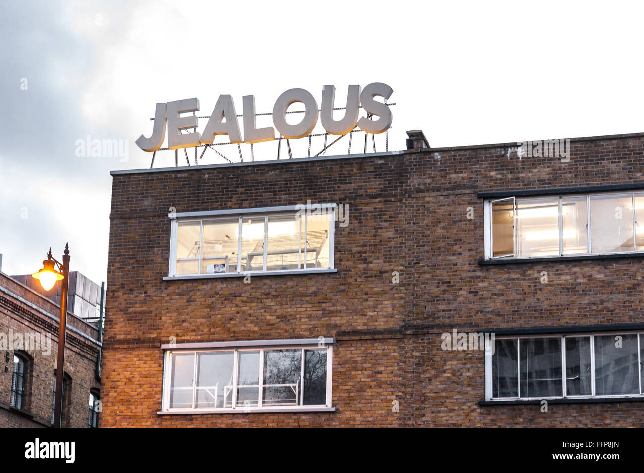 Grand panneau disant 'jaloux' sur un ancien bâtiment industriel transformé aujourd'hui en bureaux dans la zone autour de hipster Hoxton square Banque D'Images