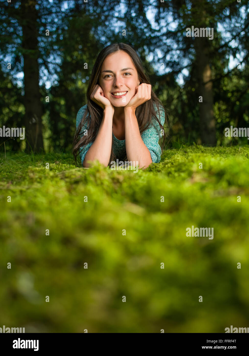 Belle jeune femme s'allonge sur l'herbe en souriant avec des bois à l'arrière-plan Banque D'Images