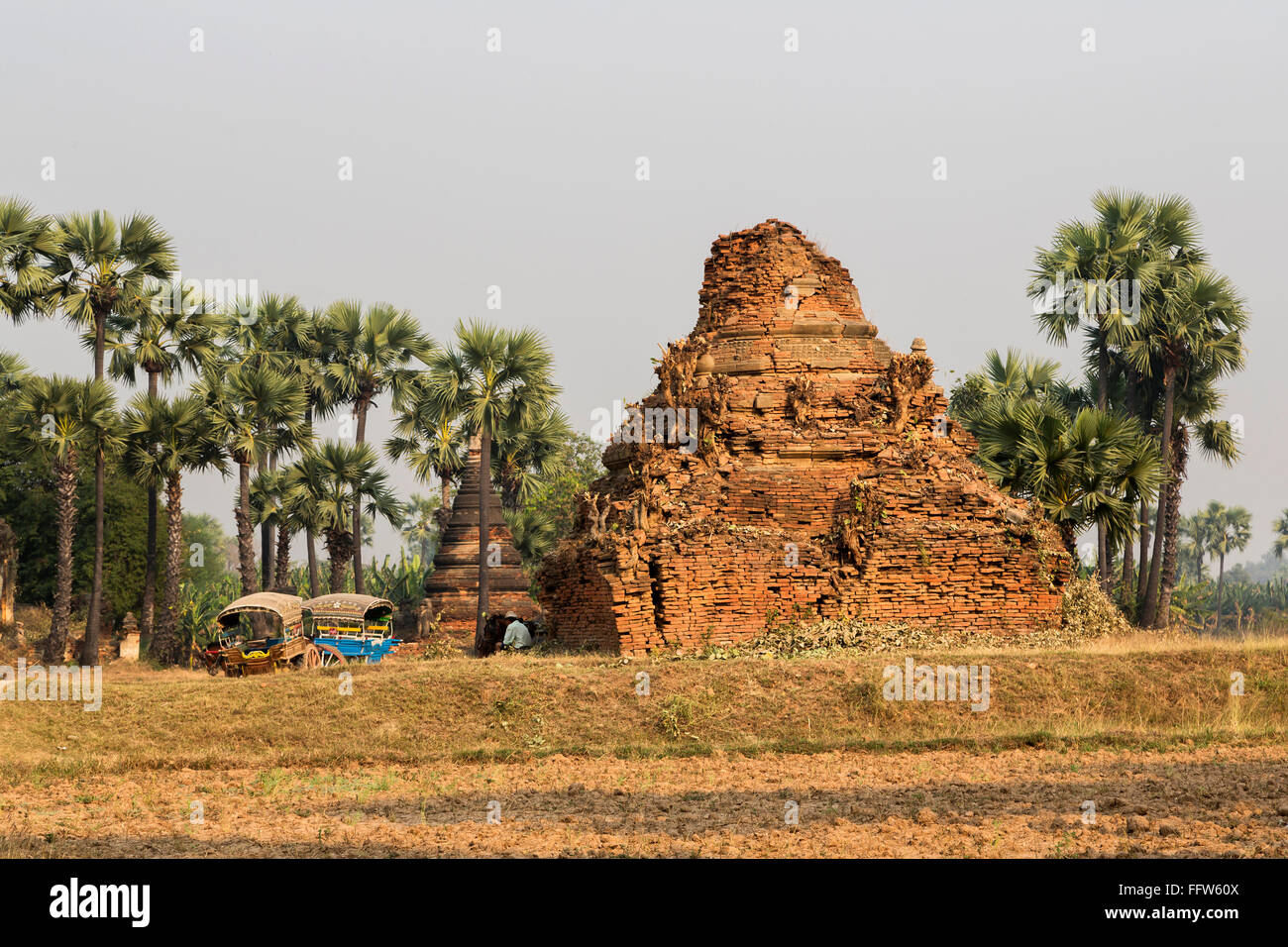 Inwa (AVA) - Les ruines de temple de briques birmanes au repos l'homme et deux charrettes colorées typiques. Banque D'Images