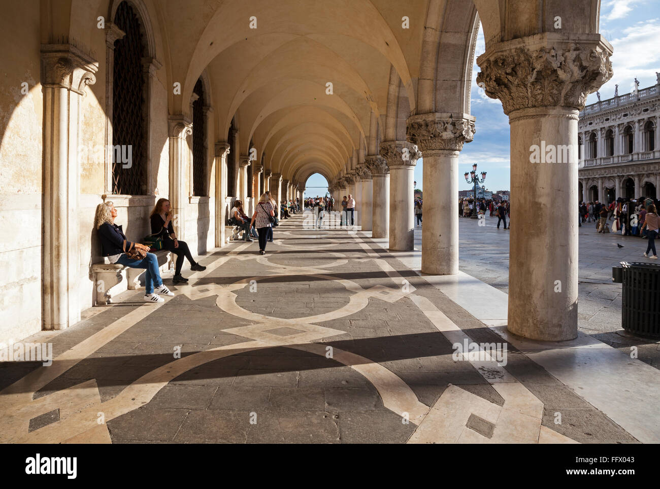 Les touristes se détendre sur les bancs et se promener le long de la colonnade du Palais des Doges, Venise, en soir sunshine Banque D'Images