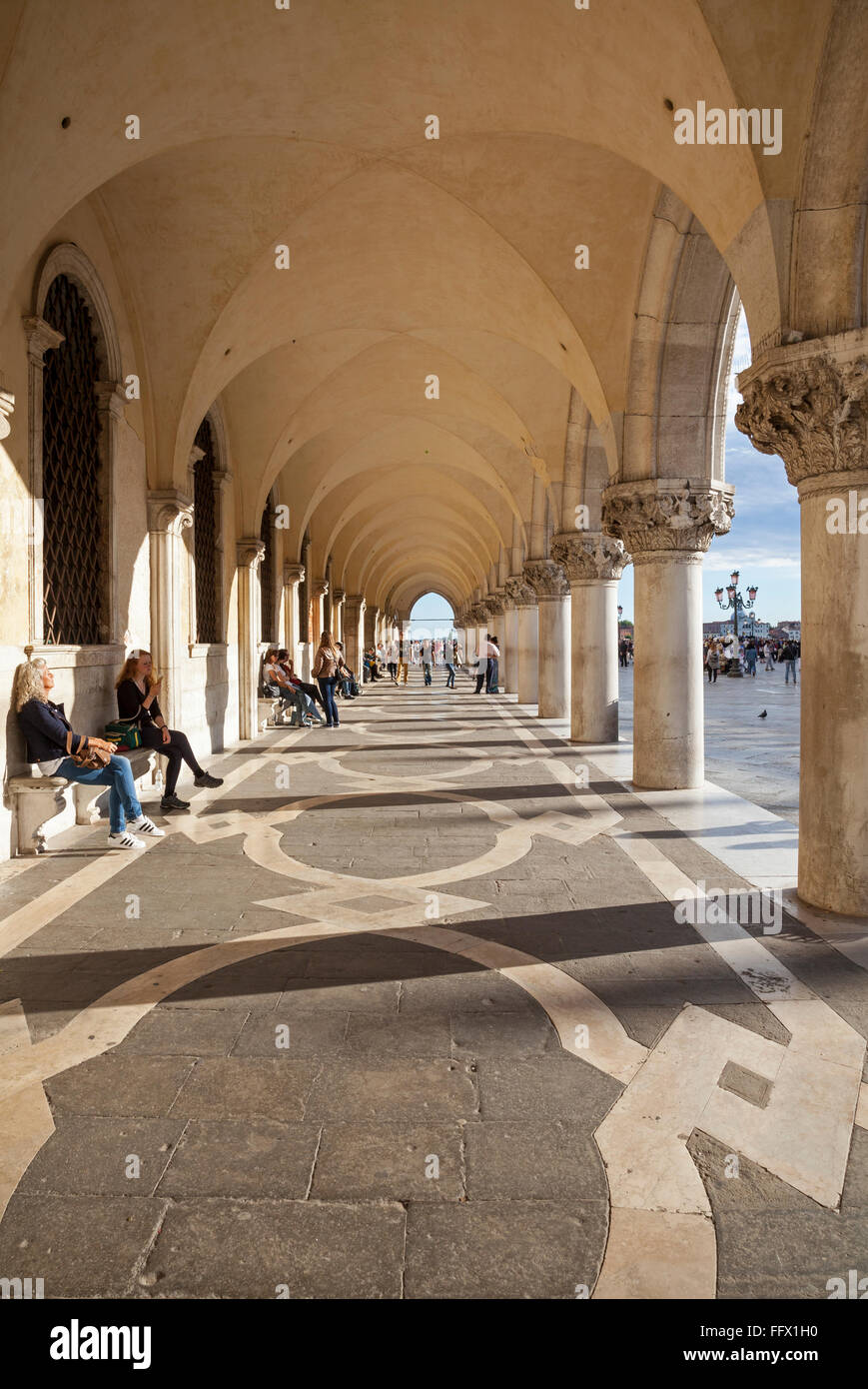 Les touristes se détendre sur les bancs et se promener le long de la colonnade du Palais des Doges, Venise, en soir sunshine Banque D'Images