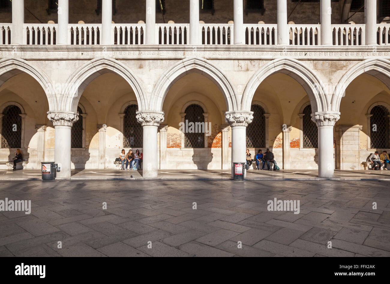 Les touristes se détendre sur les bancs et se promener le long de la colonnade du Palais des Doges, Venise, en soir sunshine Banque D'Images