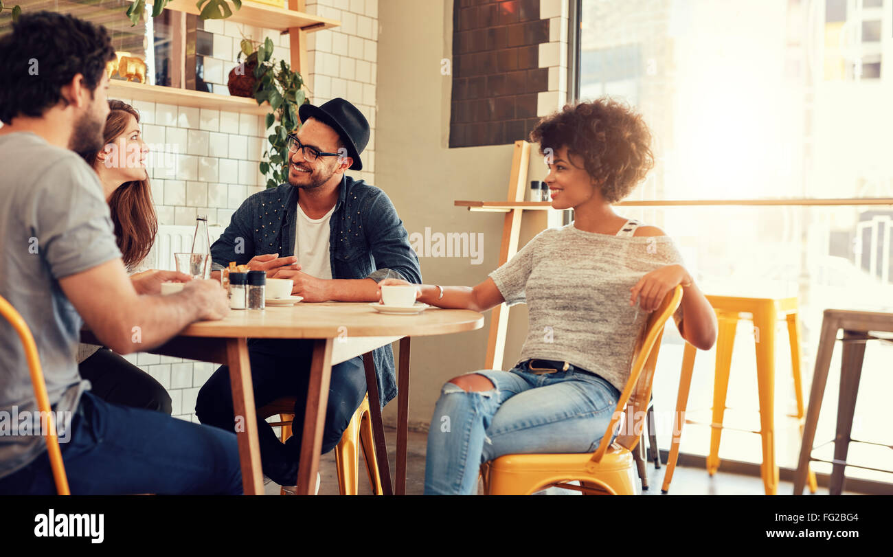 Portrait d'un jeune groupe d'amis à une réunion dans un café. Les jeunes hommes et femmes assis à table de café et de parler. Banque D'Images