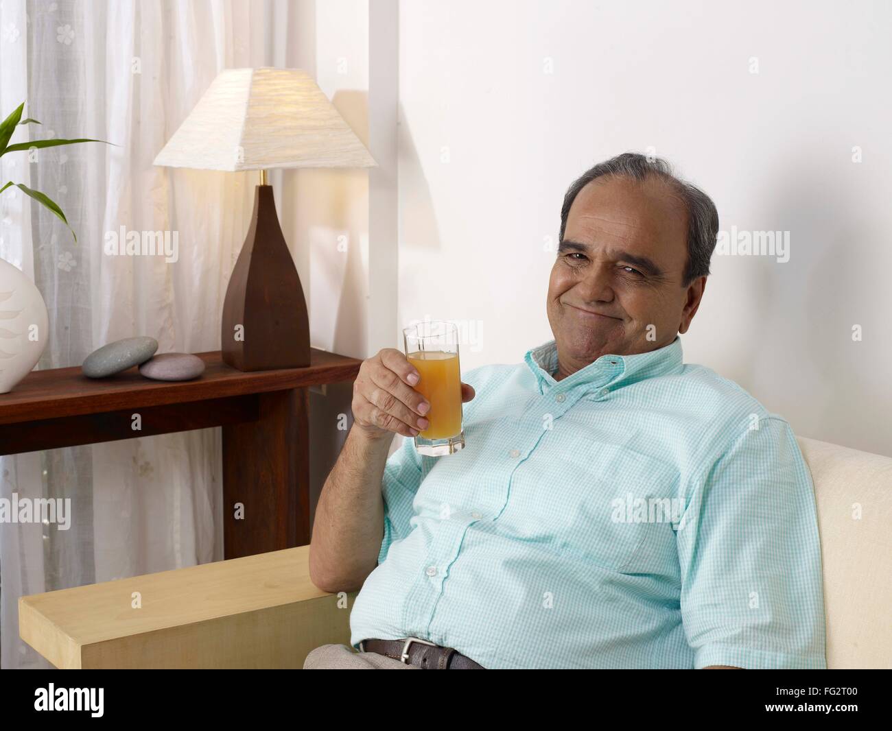 Old man holding verre de jus sitting on sofa MR# 702T Banque D'Images