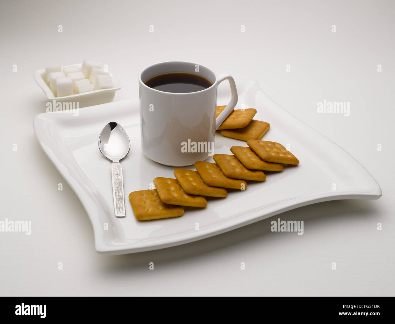 Tasse de thé noir en plat de service avec des morceaux de sucre et de biscuits en Inde Banque D'Images