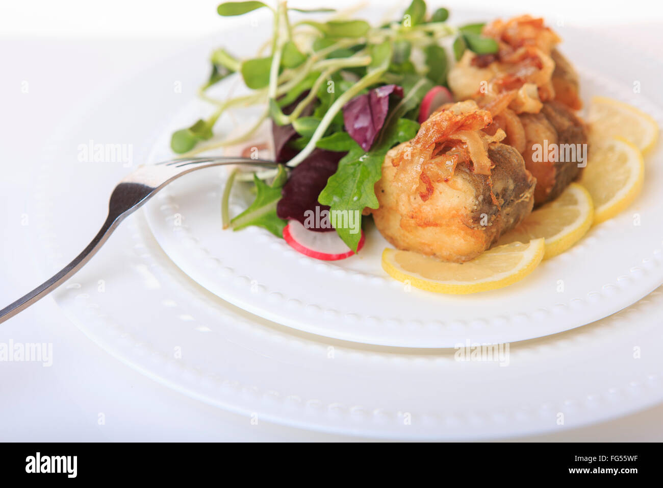 Le poisson frit avec des oignons frits, de la laitue et de citron sur une plaque blanche libre Banque D'Images