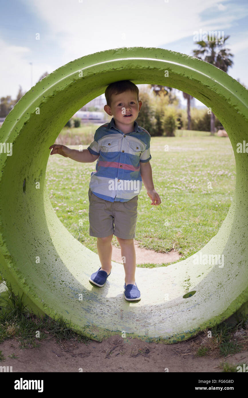 Portrait d'un enfant garçon cache l'anneau de béton et de jouer dans le parc au cours de journée d'été. Banque D'Images